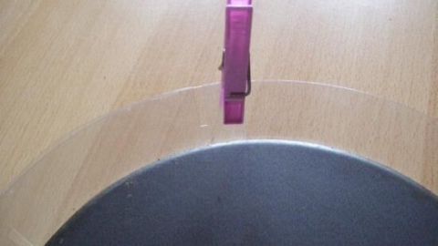Ein transparenter Tortenring wird mit einer Klammer fixiert, während er auf einem Holzuntergrund liegt.