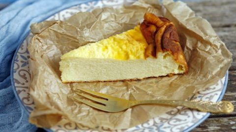 Durch das Backpapier klebt der fertige Käsekuchen nicht am Rand und sackt nicht so in der Mitte ein. Ein Stück Käsekuchen liegt auf einem Teller, umgeben von Backpapier, bereit zum Genießen in einem rustikalen Ambiente.