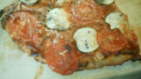 Ein Stück Pizza mit Backpulverteig liegt auf einem Holzbrett, belegt mit Tomaten und Käse, bereit zum Servieren.