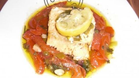 Gegrillter Lachs liegt auf warmem Tomatensalat, umgeben von einem aromatischen Olivenöl. Ein frischer Zitronenschnitz verleiht Geschmack.