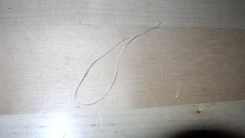 Ein Stück Zahnseide liegt auf einem hellen Holztisch und bildet eine Schlaufe, klar erkennbar auf der glatten Oberfläche.