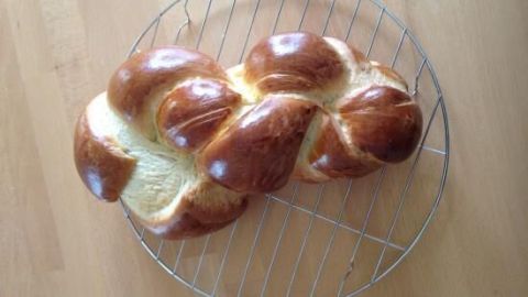 Ein Butterzopf liegt glänzend auf einem Kuchengitter, frisch gebacken, bereit zum Servieren in einer heimischen Küche.