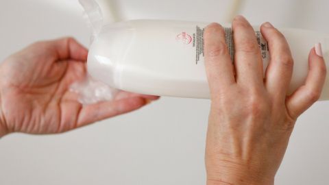 Eine Person hält eine Shampoo-Flasche, während sie versucht, überschüssiges Shampoo in die Flasche zurückzugeben.