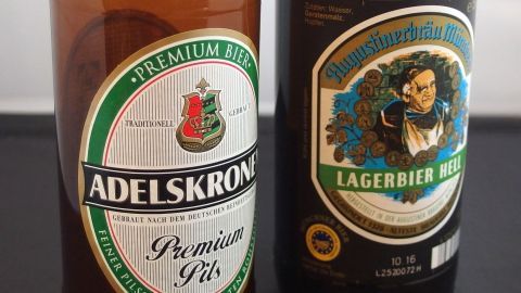 Zwei Bierflaschen stehen nebeneinander, eine mit dem Etikett „Adelskrone Premium Pils“ und die andere „Lagerbier R“ – billig, aber lecker.