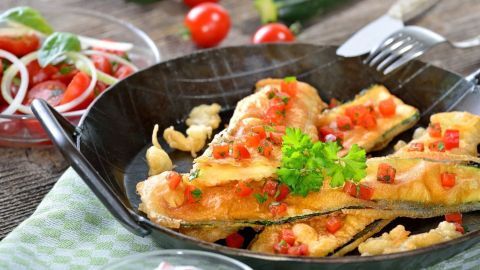 Gebratene Zucchini Schnitzel liegen auf einem Teller, garniert mit Tomaten und Petersilie, umgeben von frischem Salat.