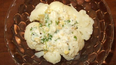 Ein Blumenkohlsalat wird in einer durchsichtigen Schüssel serviert, umgeben von einer rustikalen Tischumgebung.