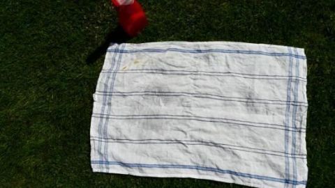 Ein rotes Ketchupflasche wird &uuml;ber ein wei&szlig;es Tuch auf gr&uuml;nem Gras gehalten, bereit, Tomatenso&szlig;e zu versch&uuml;tten.