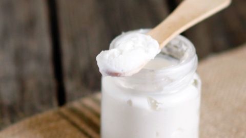 Ein Glas mit Creme für leichte Verbrennungen steht auf einem rustikalen Holzuntergrund, während ein kleiner Holzlöffel die Creme entnimmt.