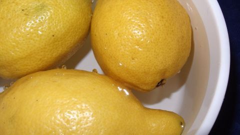 Drei frische Zitronen liegen in einer Schüssel mit Wasser, um sie haltbarer zu machen. Sie sind intensiv gelb und glänzend.