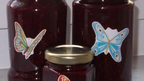 Drei Gläser mit fruchtigem Brombeermark stehen dekorativ beieinander, die Etiketten zeigen bunte Schmetterlinge.