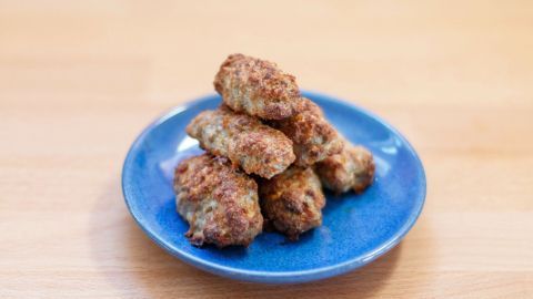 Auf einem blauen Teller liegen frisch gebackene Frikadellen, die appetitlich knusprig aussehen.