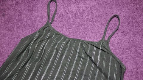 Ein grünes, gestreiftes Sportoberteil liegt auf einem lila Handtuch und wartet darauf, mit Handwäsche gereinigt zu werden.