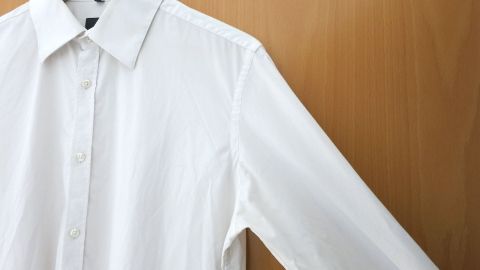 Ein weißes Hemd hängt an einem Holzkleiderbügel, bereit zum Tragen, möglicherweise mit Schweißflecken entfernt.