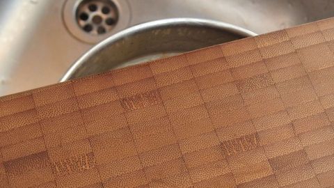 Ein Holzbrett liegt auf einem Küchenspülbecken, während sich darunter ein schmutziges Sieb befindet.