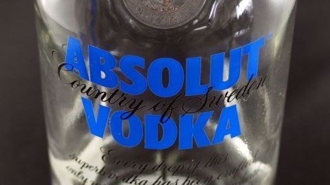 Eine Flasche Wodka steht auf einem dunklen Untergrund, umgeben von einem neutralen Raum, die klare Flüssigkeit schimmert.