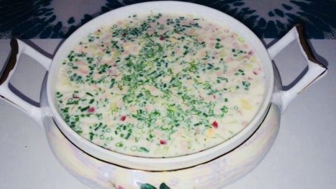 Eine Schüssel mit kühler, ungekochter Sommersuppe aus Radieschen und Gurke steht auf einem Tisch, umgeben von einem dekorativen Tuch.