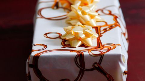 Ein hübsch verpacktes Geschenk in Tücher, geschmückt mit einer dekorativen Schleife, liegt auf einem Holztisch.