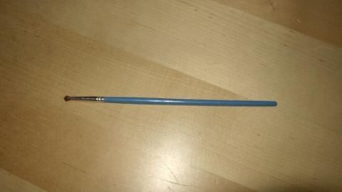 Ein feiner Pinsel liegt auf einer Holzoberfläche, geeignet als Lippen- oder Augenbrauenpinsel, um präzise Makeup-Anwendungen zu ermöglichen.