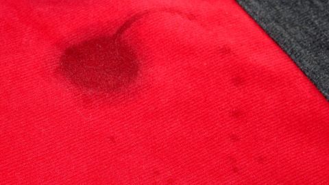 Ein rotes Kleidungsstück mit einem sichtbaren Fettfleck im Mittelpunkt, umgeben von grauem Material.