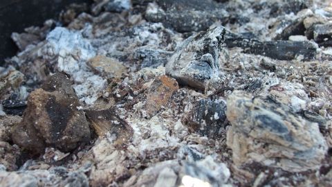 Glut und Asche liegen in einem Grillbehälter. Sand wird verwendet, um die Grillglut zu löschen und zu sichern.