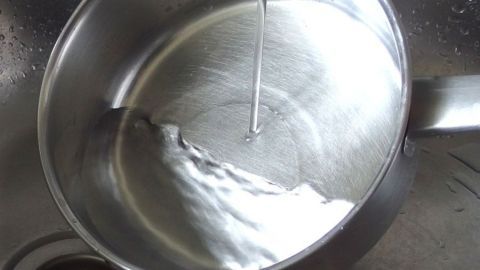 Wenn man den Kochtopf vor dem Milchkochen gut mit kaltem Wasser ausspült, brennt die Milch nicht an. Ein kochender Topf mit Wasser steht in der Spüle. Wasser fließt hinein, um angebrannte Milch zu vermeiden.