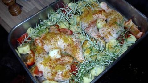 Zartes Hähnchen liegt mit Rosmarin-Kartoffeln und frischen Kräutern in einer Backform, bereit zum Braten.