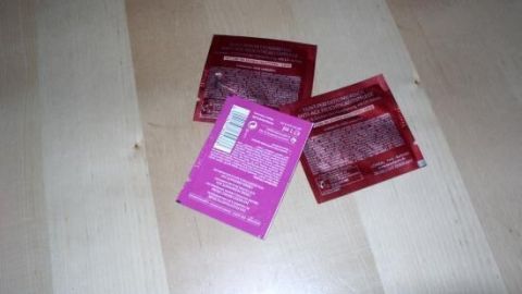 Drei Pflegeproben für Hals und Dekolleté liegen auf einem hellen Holztisch, bereit zur Anwendung.