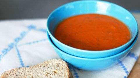 Suppe zu salzig geraten? Mithilfe eines altbackenen Brötchens oder einer Scheibe Weißbrot die Suppe "entsalzen". Eine blaue Schüssel mit roter Suppe steht auf einem Tisch, daneben liegt ein Stück Brot, ideal für eine Mahlzeit.