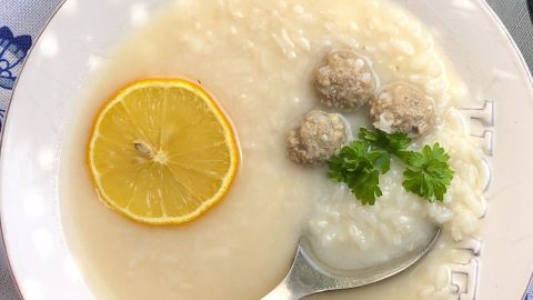 Ein Löffel mit Reis und kleinen Fleischbällchen wird in eine klare Suppe mit Zitronenscheibe und Petersilie eingetaucht.