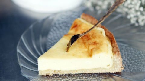 Ein Käsekuchen steht auf einem eleganten Tortenständer, während ein Stück auf einem Teller zusammen mit einem Silberlöffel serviert wird.
