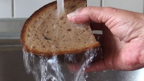 Ein Stück trockenes Brot wird unter fließendem Wasser gehalten, um es wieder genießbar zu machen.