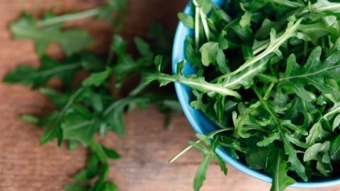 Frischer Rucola liegt in einer blauen Schüssel und wird auf einem Holztisch zubereitet, ideal für Spinatgerichte.