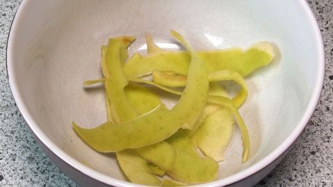 Ein weißer Schüssel enthält grüne Apfelschalen, die ordentlich zusammengerollt sind und auf einer hellen Oberfläche liegen.
