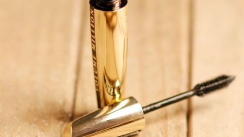 Eine Goldfarbene Wimperntusche liegt auf einem Holzuntergrund, bereit für die Anwendung, um Wimpern zu betonen.