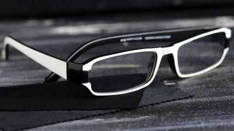 Alles was man zum Brille putzen benötigt, ist ein fließendes Wasser und ein Tropfen Spülmittel. Schwarze und weiße Brille liegt auf einem grauen Untergrund, bereit zum Putzen für eine klare Sicht.