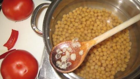 Gekochte Kichererbsen in einem Topf, während Tomaten daneben bereitliegen, um Hummus zuzubereiten.
