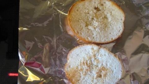 Brötchenhälften liegen auf Alufolie und werden auf einer Glaskeramikherdplatte geröstet, um knusprige Brotscheiben zu erhalten.