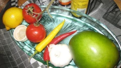 Frische Zutaten wie Mango, Chili, Tomaten und Zitrone liegen auf einem gläsernen Teller, bereit für die Würzige Mango-Chili-Sauce.