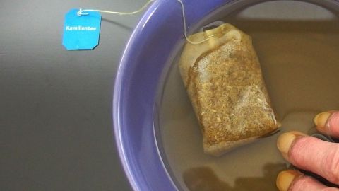 Ein Teebeutel liegt in einer Schüssel mit Wasser, während eine Hand ihn leicht bewegt, um die Nagelbettentzündung zu lindern.
