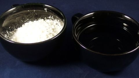 Ein schwarzer Behälter mit Speisestärke sitzt neben einem leeren, schwarzem Becken; beide stehen auf einem blauen Untergrund.