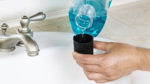 Eine Person gießt blaue Listerine Mundspülung in einen Messbecher neben einem Waschbecken auf einem Badezimmerwaschtisch.