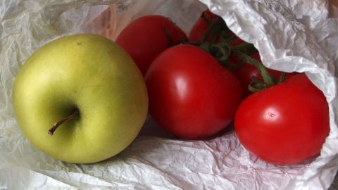 In einer durchsichtigen Tüte liegen reife Tomaten und ein grüner Apfel, die in einer Küche auf einem Tisch platziert sind.
