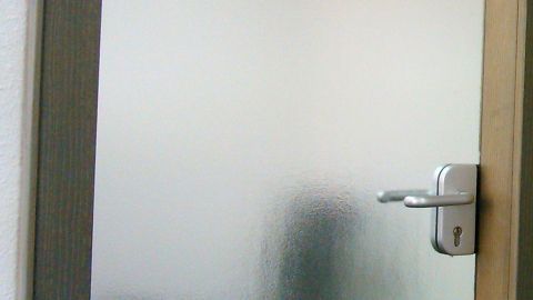 Eine Glastür mit Struktur befindet sich im Fokus, während sie gereinigt wird. Der Hintergrund bleibt unscharf.