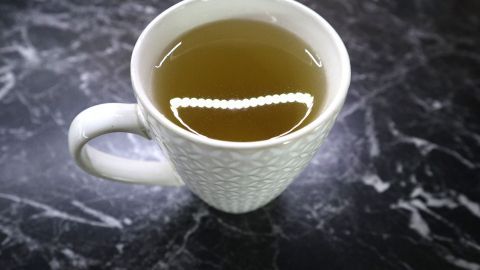 Eine Tasse mit grünem Tee steht auf einer marmorierten Oberfläche und reflektiert leichtes Licht, das den Inhalt betont.