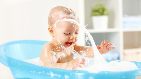 Ein Baby planscht fröhlich in einer blauen Badewanne, umgeben von einer hellen und freundlichen Umgebung.