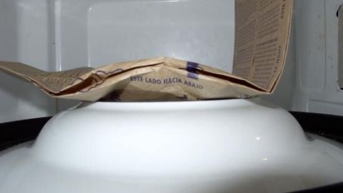 Ein Mikrowellen-Popcorntütchen steht auf einem weißen Teller in der Mikrowelle und ist bereit zum Poppen.