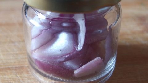 Ein kleines Glasgefäß mit geschnittenen Zwiebeln, das auf einer Holzoberfläche steht, erzeugt einen Zwiebelgeruch.