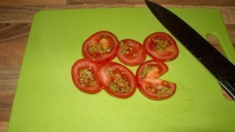 Im Artikel "Pesto küsst Tomate" wird gezeigt, wie frische Tomatenscheiben perfekt mit Pesto kombiniert werden können. Diese einfache Zubereitung bringt den Geschmack des Sommers direkt auf deinen Teller. Probiere es aus! Auf einem grünen Schneidebrett liegen frisch geschnittene Tomaten, während ein Küchenmesser daneben platziert ist.