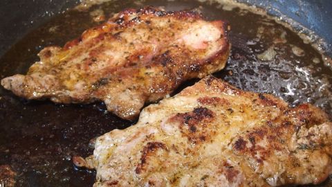 Zwei Nackenkoteletts braten in einer Pfanne, umhüllt von goldbrauner Kruste und leckerer Marinade aus schwarzem Tee.