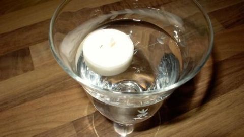 Eine Schwimmkerze bleibt auf der Wasseroberfläche eines Glases, das auf einer Holzoberfläche steht.